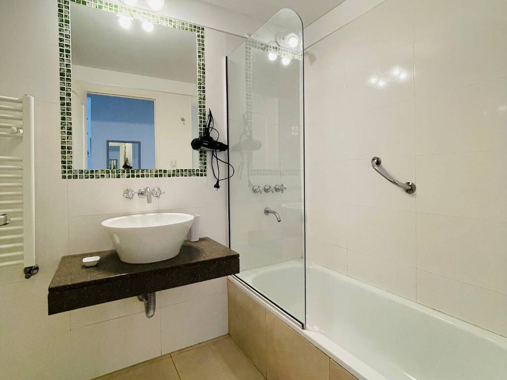 Baño con bacha de apoyo, espejo y bañera con mampara