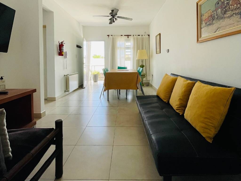 Sillón negro con almohadones amarillos y mesa al fondo