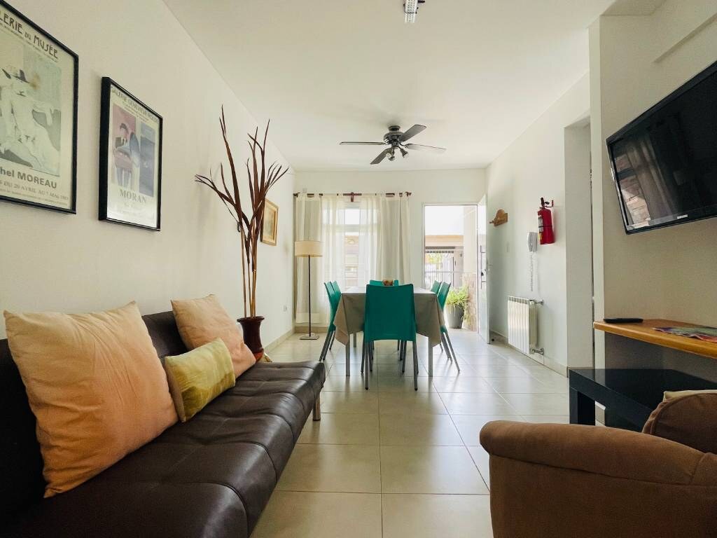 Living con sillón de cuero, almohadones y mesa con sillas turquesa al fondo